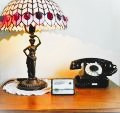 Stylowa lampa witrażowa w stylu Tiffany na drewnianym stoliku obok czarnego telefonu retro z tarczą, całość oświetlona ciepłym światłem