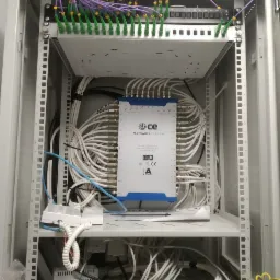 Otwarta szafa rack z multiswitchem CE 9/32 HD, licznymi kablami koncentrycznymi, patch panelem z fioletowymi i zielonymi kablami ethernet oraz elementami instalacji wewnątrz, widoczne oznaczenia...