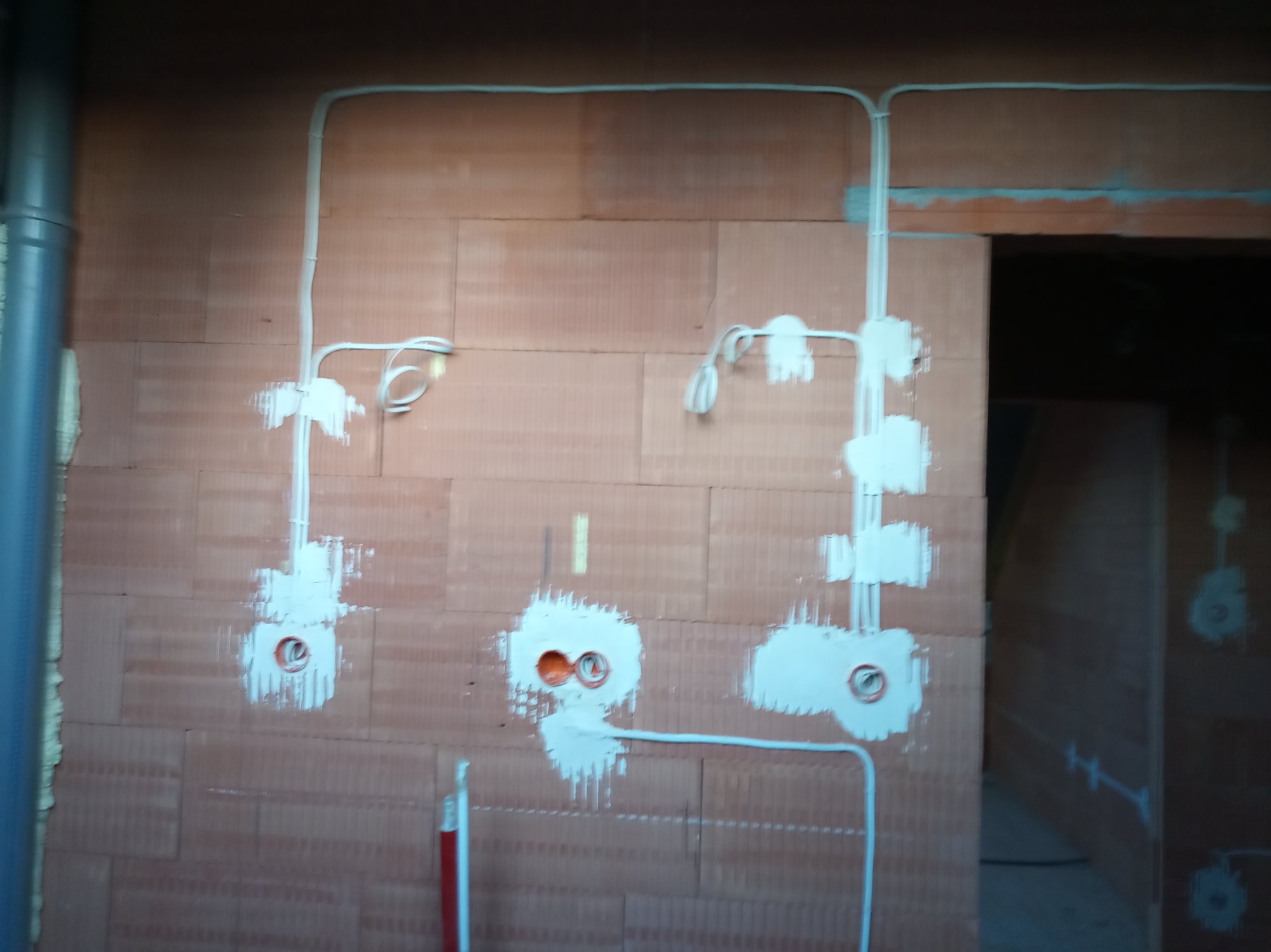 Instalacja elektryczna w trakcie prac: przewody poprowadzone po ścianie z cegły, puszki elektryczne zamontowane i obrobione gipsem, widoczne fragmenty peszli.