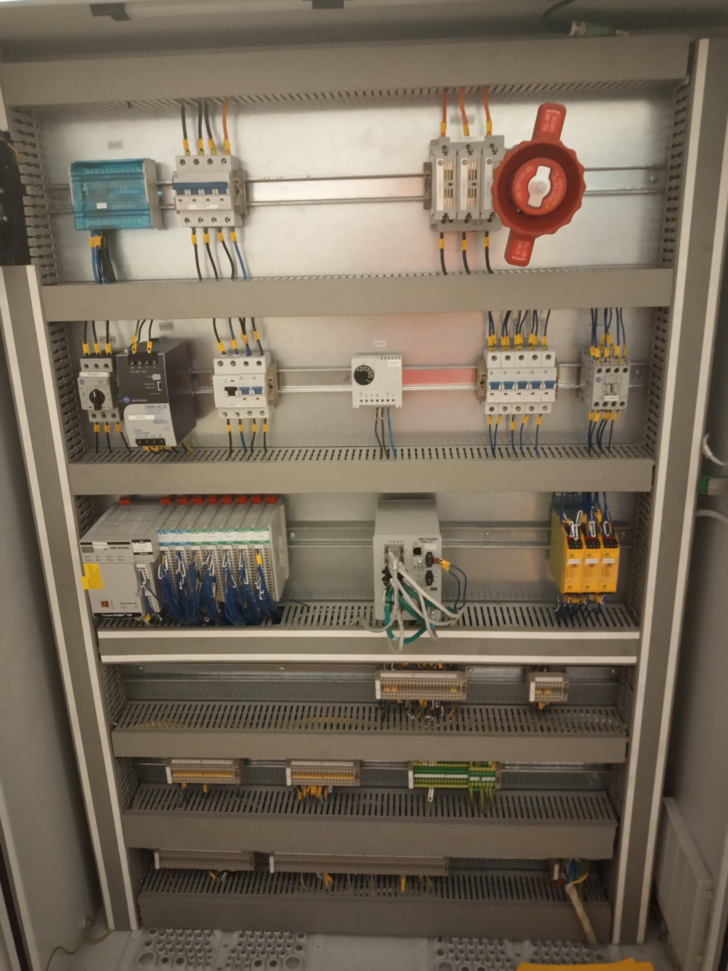 Wnętrze szafy sterowniczej z modułami, bezpiecznikami i okablowaniem, widok na ułożone poziomo rzędy komponentów elektrycznych w metalowej obudowie.