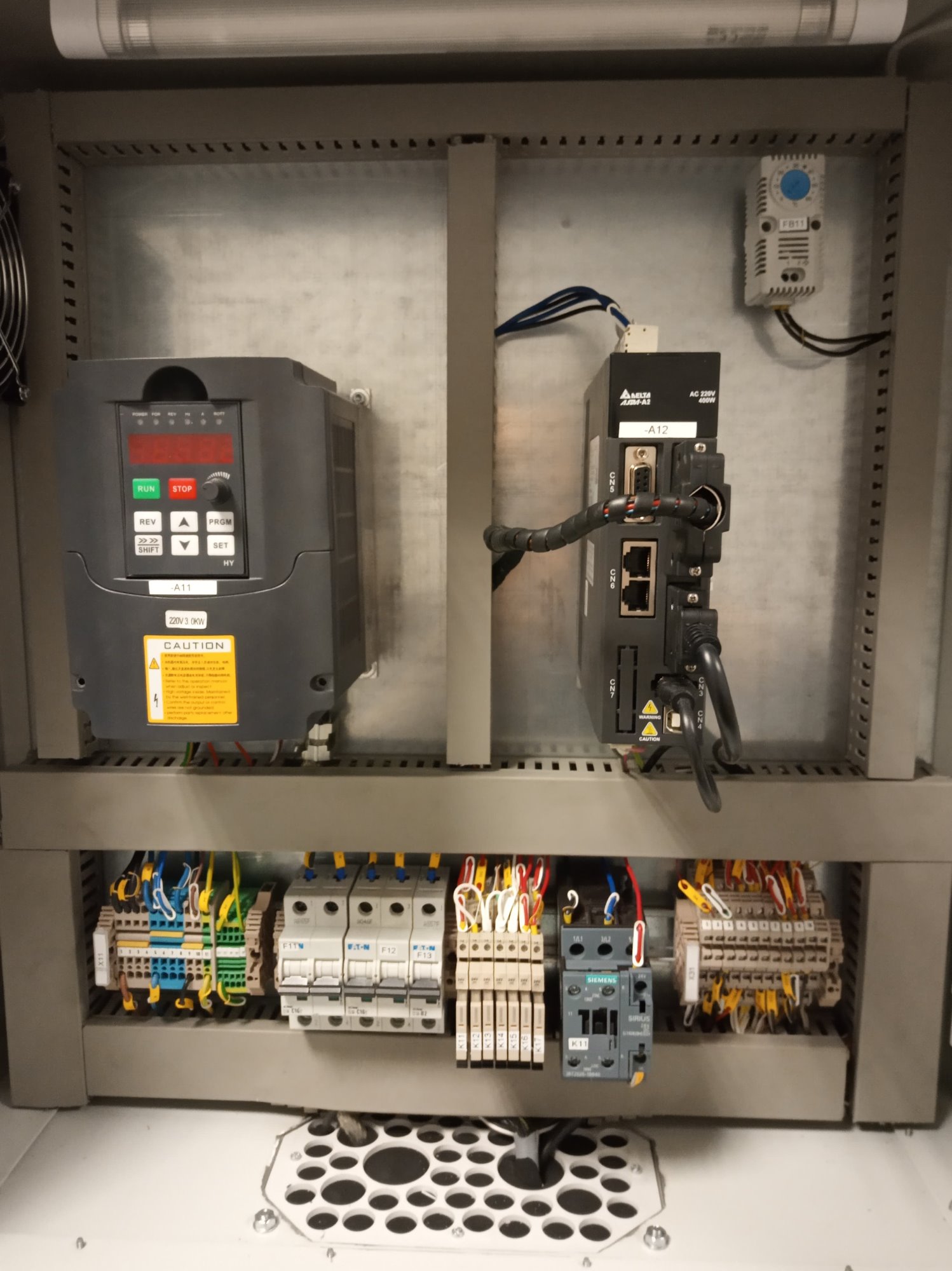 Wnętrze szafy sterowniczej z zamontowanym falownikiem Delta, sterownikiem PLC, bezpiecznikami i okablowaniem, widoczne oznaczenia A11, A12, F11, F12, F13, K11, X11, FB11.