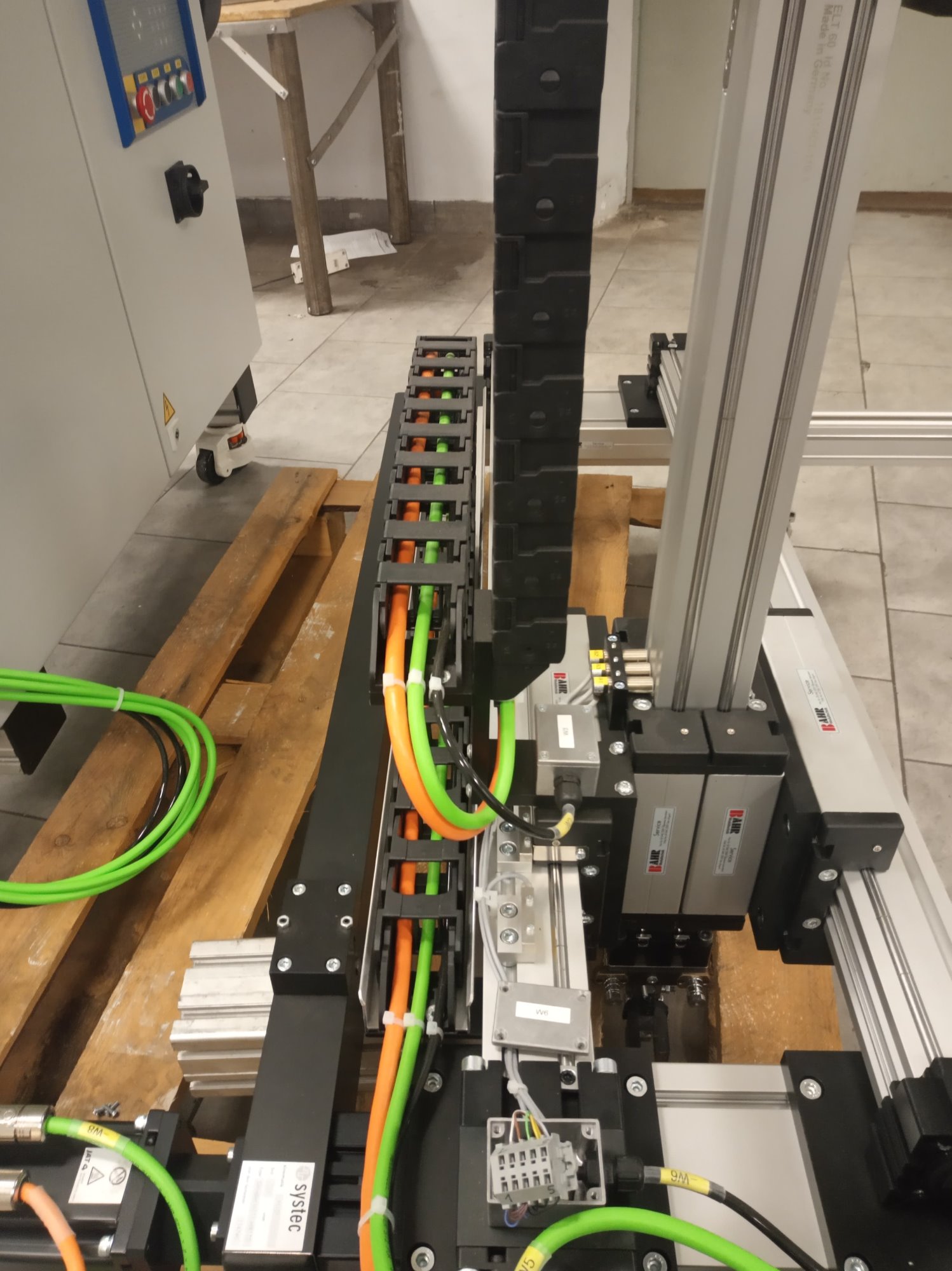 Szczegółowe ujęcie konstrukcji maszyny z widocznymi przewodami w prowadnicach kablowych, elementami pneumatycznymi i aluminiowymi profilami nośnymi.