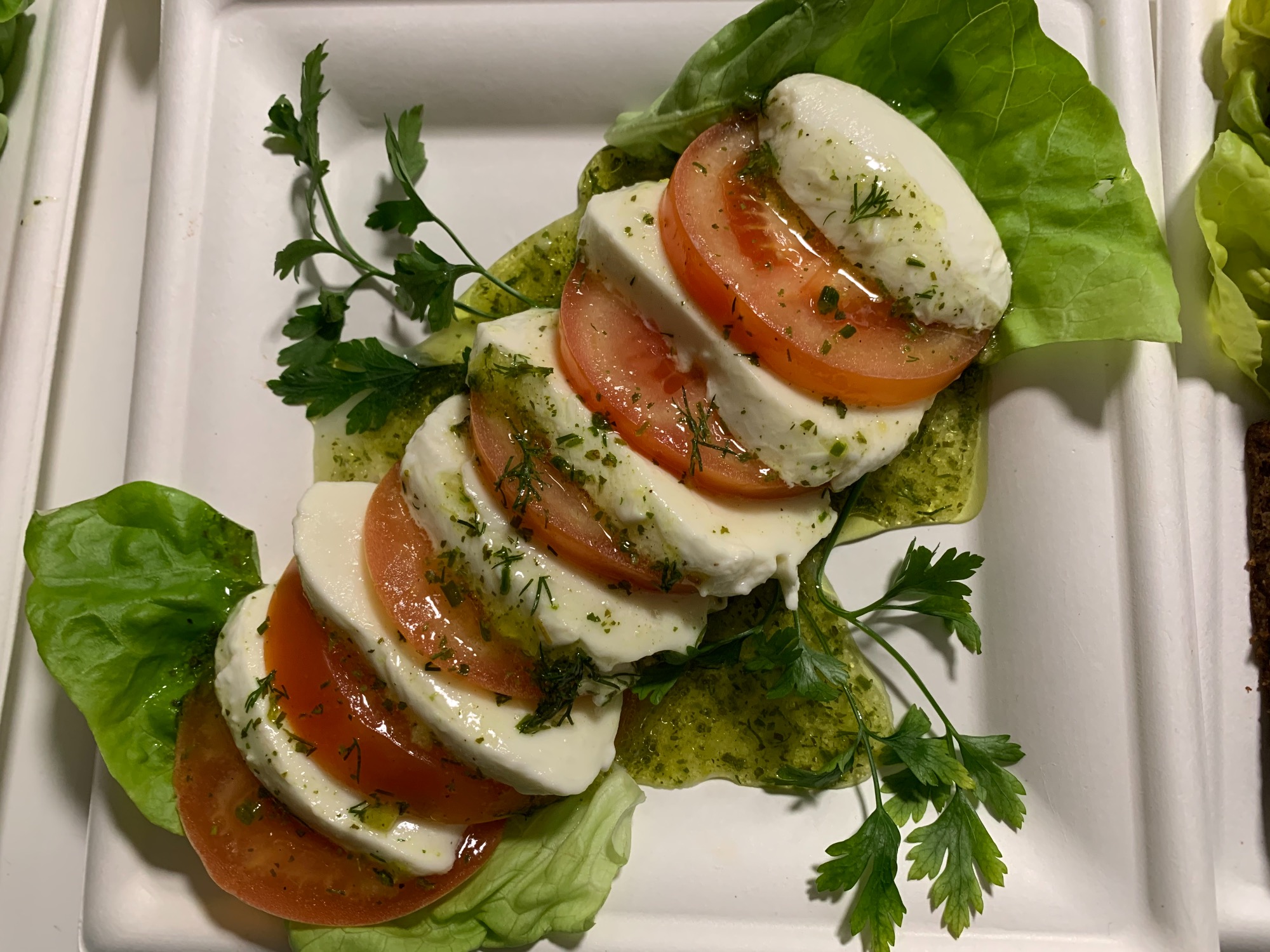 Caprese sałatka z pomidorami, mozzarellą i pesto, podana na liściach sałaty na białym talerzu.