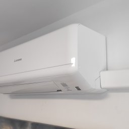 aceco Wojciech Szewczyk - Biała jednostka wewnętrzna klimatyzacji Mitsubishi zamontowana na ścianie w pomieszczeniu, widoczna instalacja elektryczna w białej listwie.