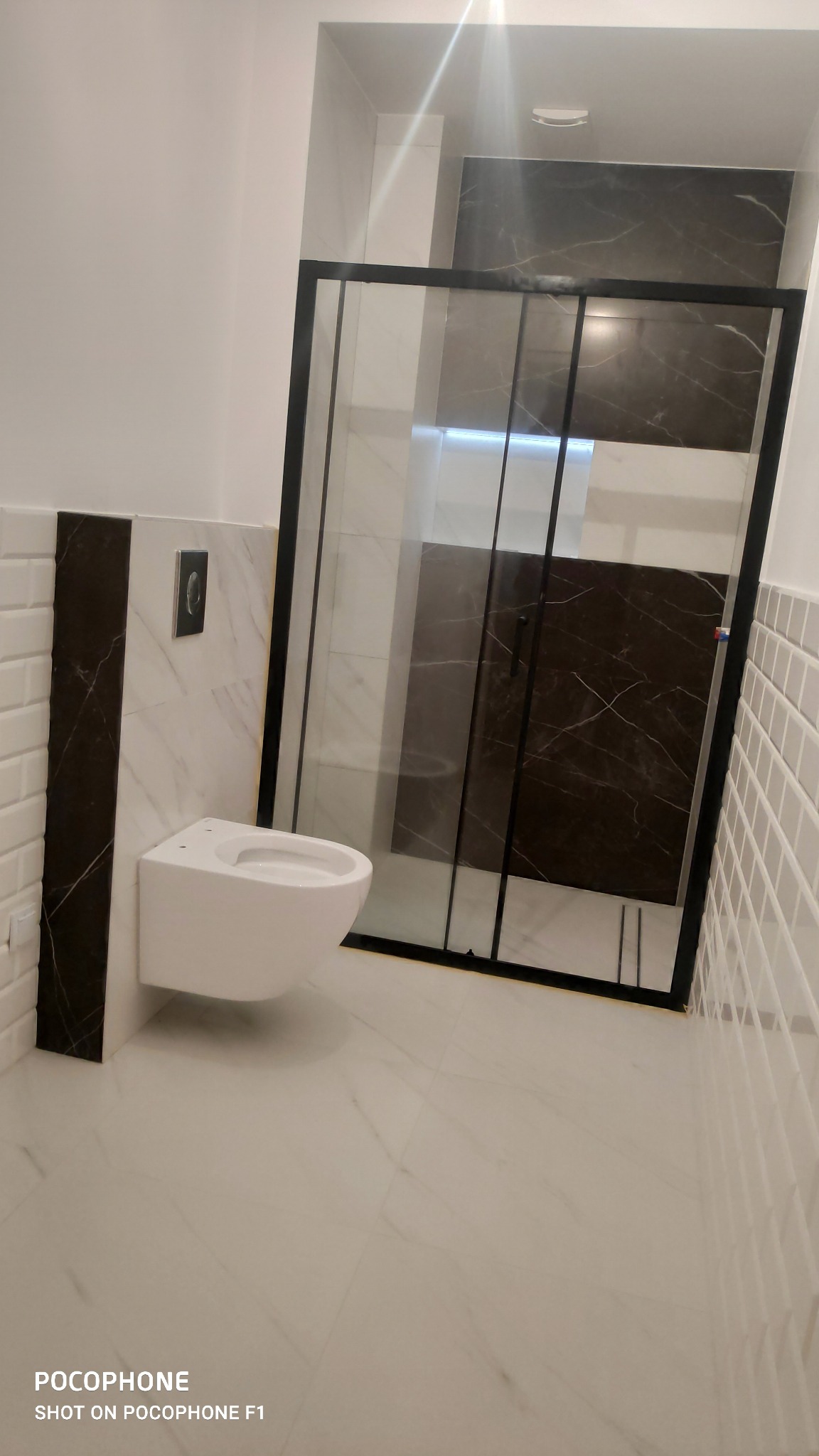 Nowoczesna łazienka z podwieszaną toaletą i czarną kabiną prysznicową z marmurowym wykończeniem ściany wewnątrz.