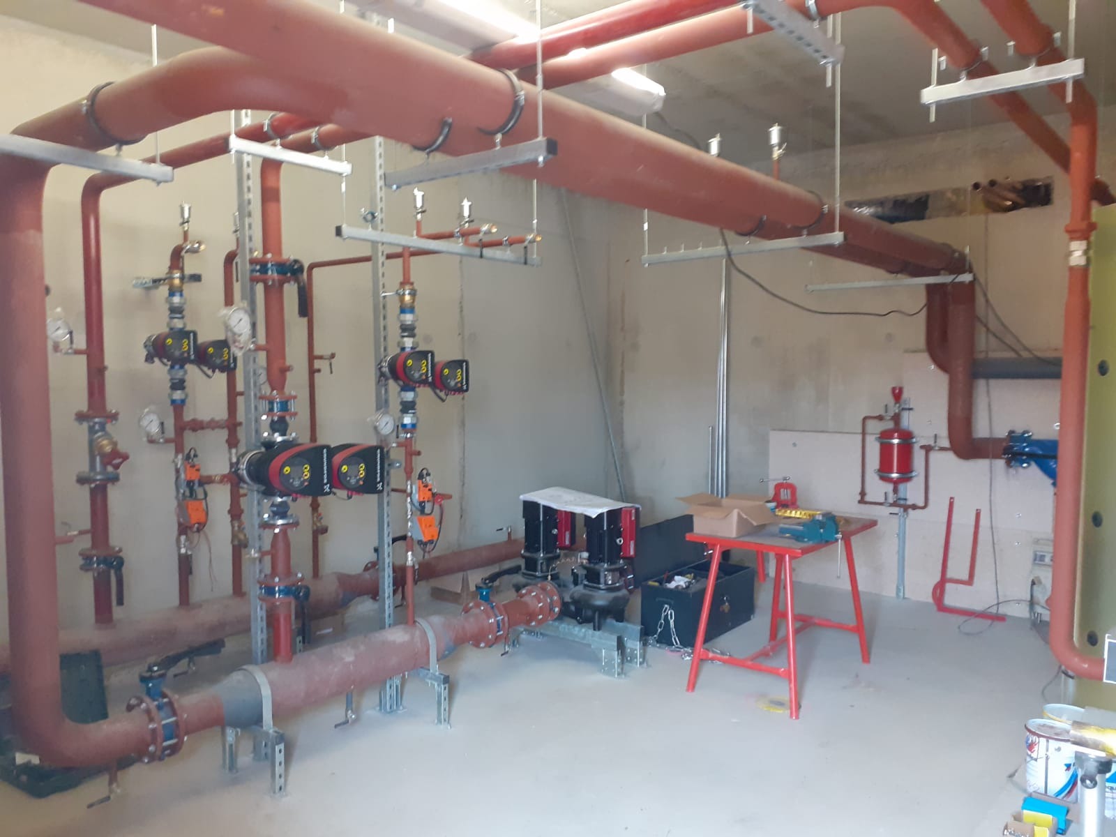 Instalacja centralnego ogrzewania w kotłowni: czerwone rury, zawory, manometry i pompy obiegowe w nowym budynku.