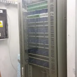 Szara szafa rack z widocznymi panelami krosowniczymi i kablami, zainstalowana w pomieszczeniu technicznym.