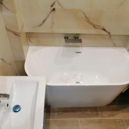 Dawid K - Wykończona łazienka z owalną wanną, umywalką z chromowaną baterią i beżowymi płytkami imitującymi marmur na ścianach.