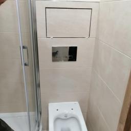 Dawid K - Wykończona łazienka z beżowymi płytkami, kabiną prysznicową narożną z chromowanymi okuciami, podwieszanym WC i ukrytym dostępem rewizyjnym.