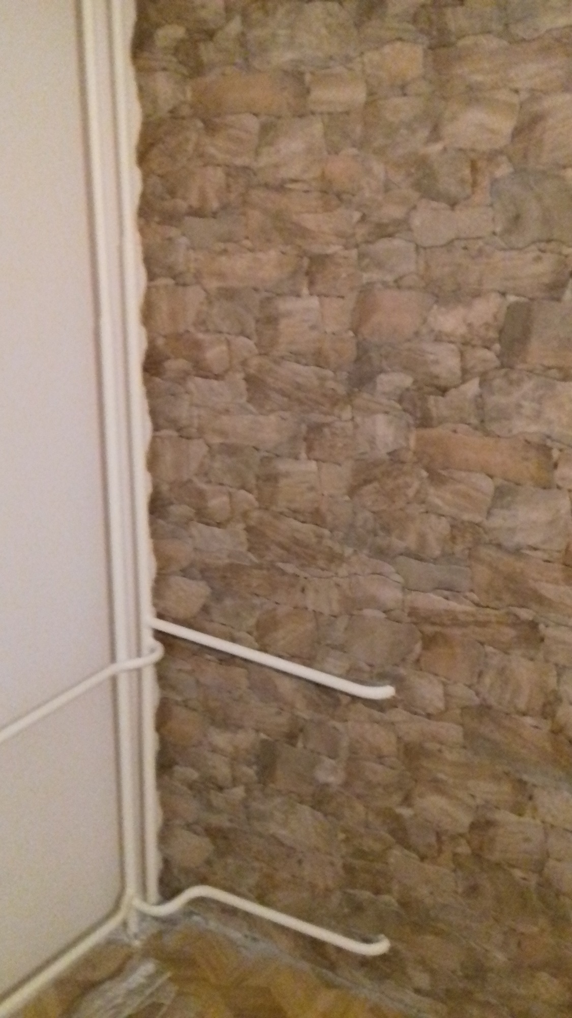 Ściana z kamienia dekoracyjnego z widoczną instalacją grzewczą i fragmentem białych drzwi.