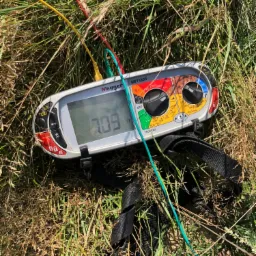 Miernik Megger MFT1835 leżący w trawie podczas pomiarów, z widocznymi przewodami pomiarowymi w kolorach: czerwonym, żółtym i zielonym, wyświetlający wynik 7.09 Ω.