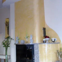 Wykończony salon z kominkiem obudowanym granitem, ściany pomalowane farbą strukturalną w odcieniach żółci, dekoracje na półce kominkowej.