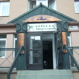 Wejście do oddziału KOPEX S.A. w Lubinie, widoczne schody, otwarte szklane drzwi, zielona konstrukcja nad wejściem z logo ENGRAM, na ścianie budynku widoczne logo HIP-BUD.