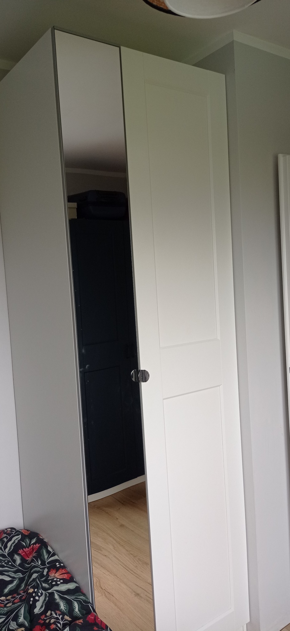 Biała szafa z lustrzanymi drzwiami, widoczna część wnętrza szafy i podłoga. Minimalistyczny design.