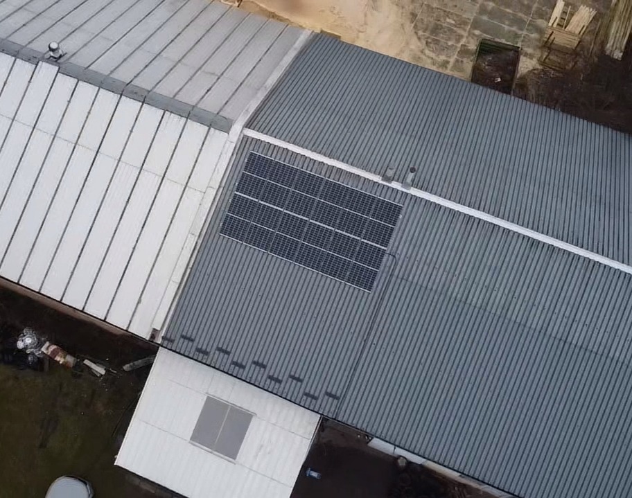 Widok z góry na zamontowane panele słoneczne na szarym, blaszanym dachu budynku przemysłowego z widocznymi elementami konstrukcyjnymi.