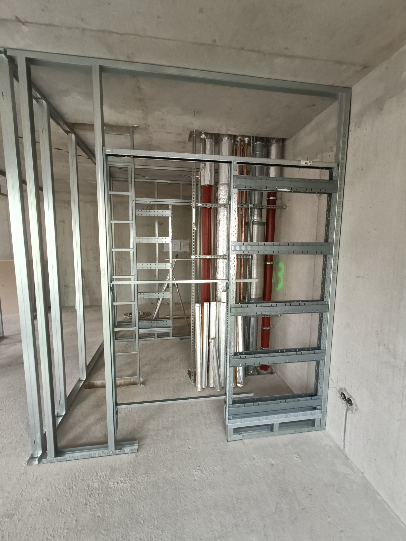 Metalowa konstrukcja szkieletowa ścian działowych w surowym stanie, widoczne instalacje wentylacyjne i elektryczne w tle, przygotowane do dalszych prac wykończeniowych.