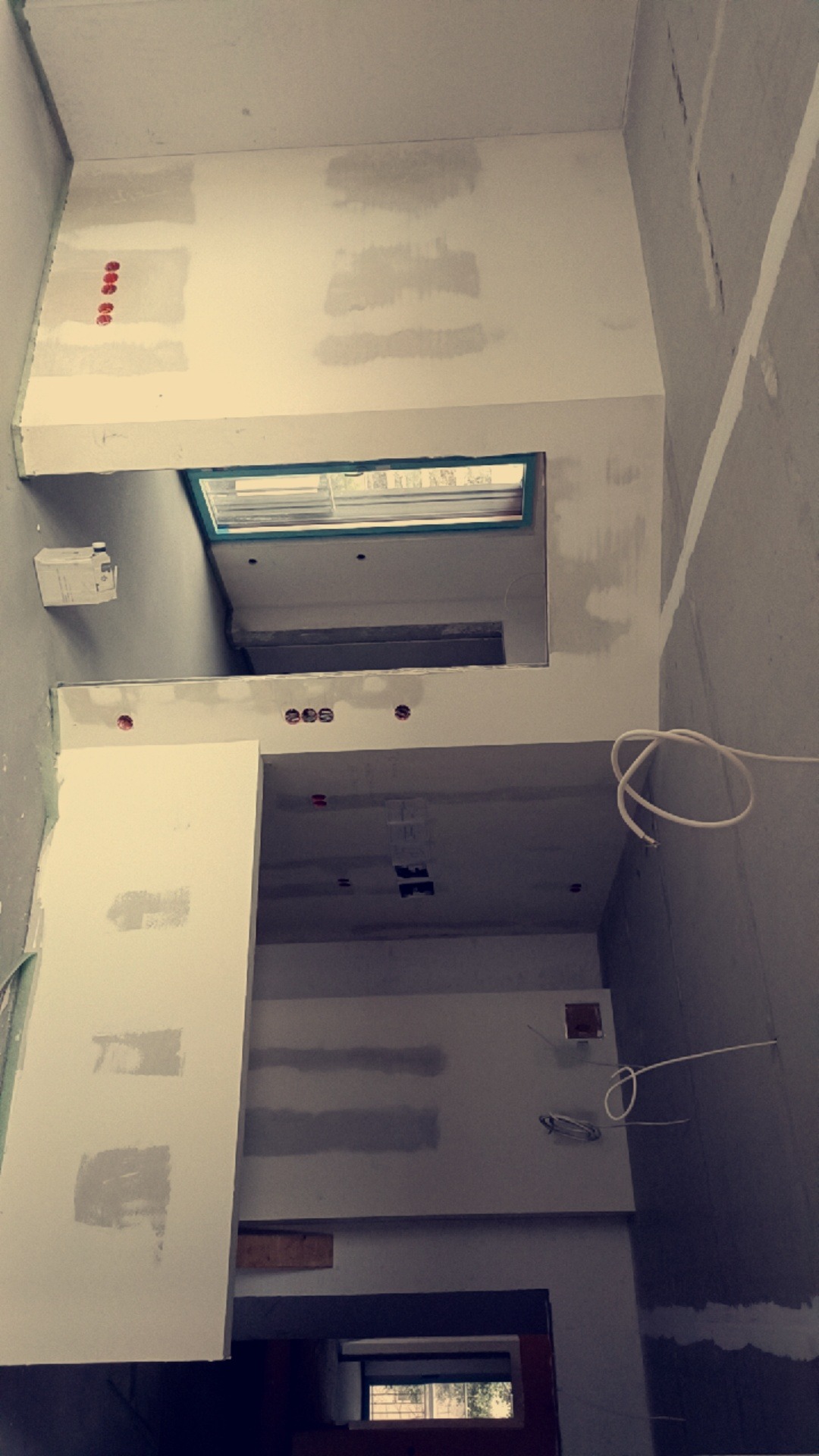 Wnętrze w trakcie wykańczania: ściany z widocznymi fragmentami nałożonej gładzi, otwory na gniazdka elektryczne i okno dachowe z zieloną ramą.