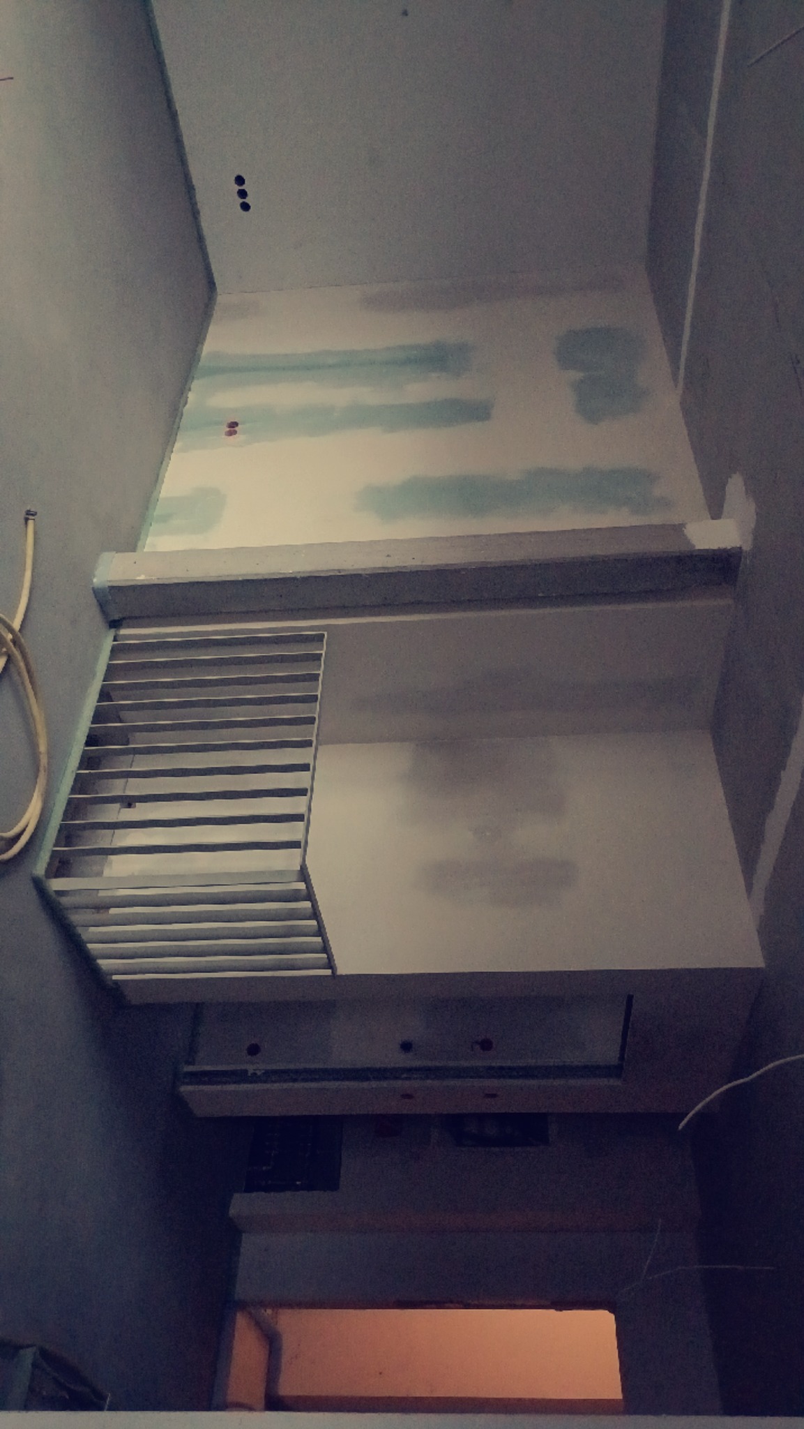 Wnętrze w trakcie prac wykończeniowych: ściany z widocznymi łączeniami płyt, częściowo pokryte masą szpachlową, widoczna konstrukcja metalowa, prawdopodobnie wentylacyjna.