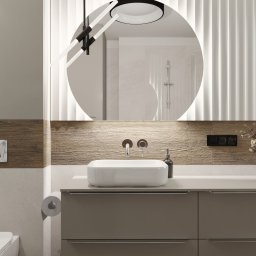 STUDIO ZMIANA - Nowoczesna łazienka z okrągłym lustrem podświetlanym LED, białą umywalką nablatową, szarobrązowymi szafkami, drewnopodobną okładziną ścienną i dekoracyjnymi panelami ściennymi. Widoczne również...