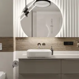 Nowoczesna łazienka z okrągłym lustrem podświetlanym LED, białą umywalką nablatową, szarobrązowymi szafkami, drewnopodobną okładziną ścienną i dekoracyjnymi panelami ściennymi. Widoczne również...