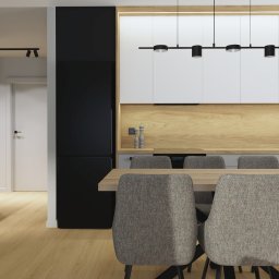 STUDIO ZMIANA - Nowoczesna kuchnia z jadalnią: białe szafki górne, drewniany panel ścienny, szare szafki dolne, czarna lodówka, stół z szarymi krzesłami, oświetlenie punktowe i wiszące lampy.