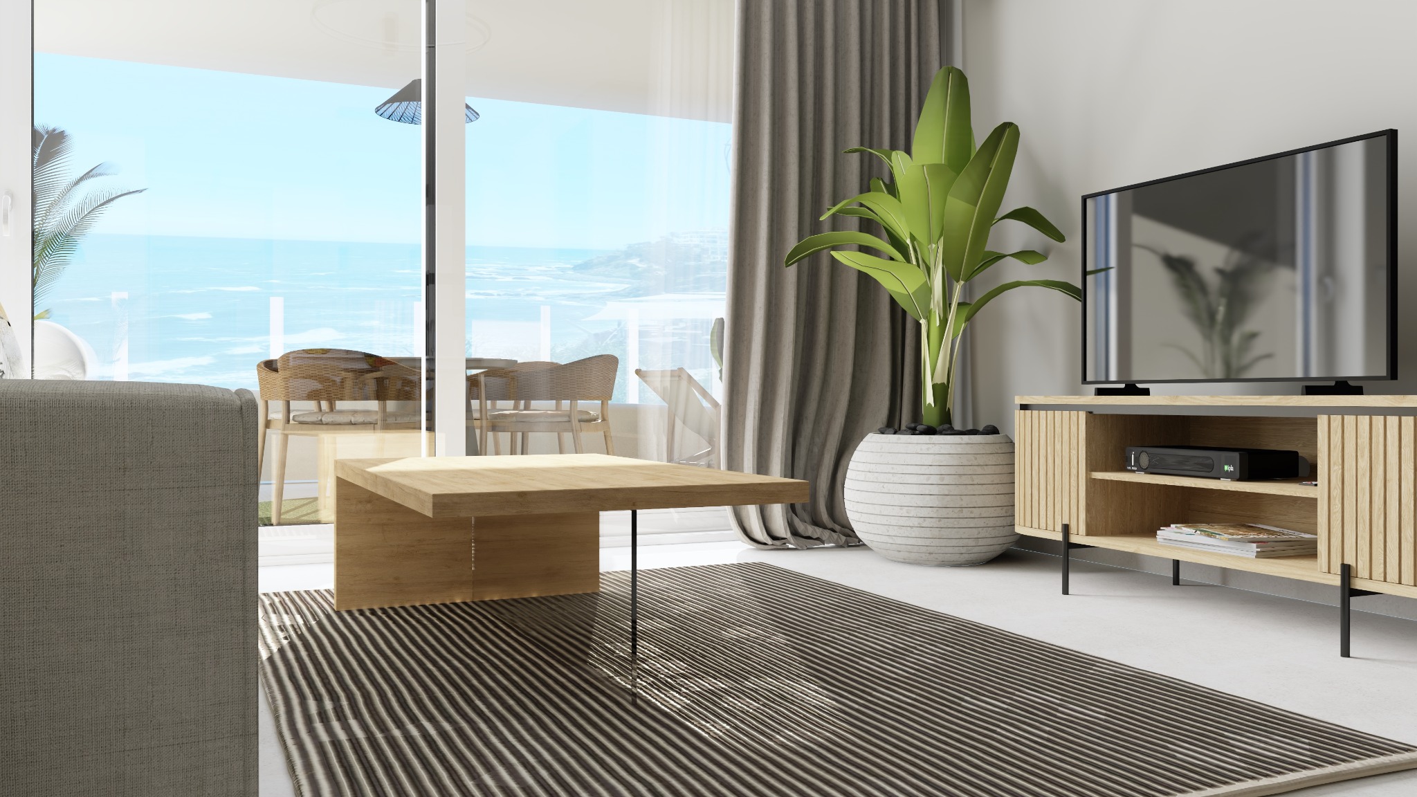 Jasne wnętrze salonu z widokiem na morze, drewniany stolik kawowy, szafka RTV z rośliną w donicy, szaro-biały dywan w paski, szara sofa częściowo widoczna po lewej stronie.