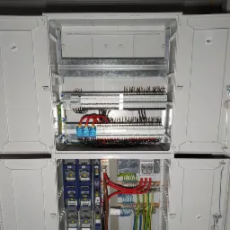 Otwarta, dwuczęściowa rozdzielnica elektryczna w trakcie montażu, widoczne przewody, bezpieczniki i inne komponenty.