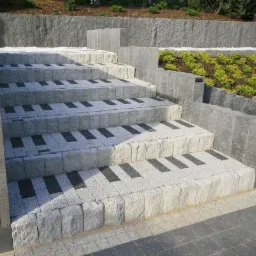 Kamienne schody zewnętrzne z elementami dekoracyjnymi przypominającymi klawiaturę fortepianu, otoczone szarą kostką i zielenią.