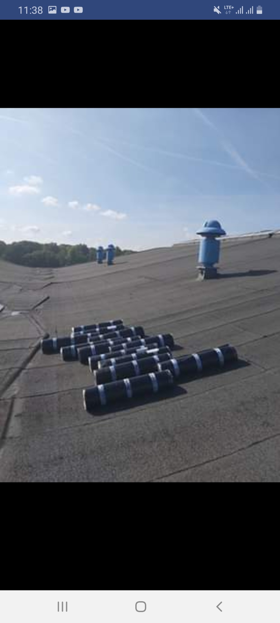 Czarny dach pokryty papą termozgrzewalną w rolkach, przygotowany do montażu, z niebieskimi kominkami wentylacyjnymi w tle pod błękitnym niebem.