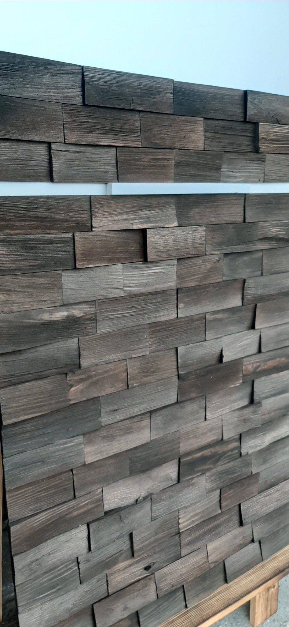 Panel ścienny z łupanych desek drewnianych w odcieniach szarości i brązu, ułożonych asymetrycznie, z widoczną strukturą drewna i delikatnymi nierównościami.