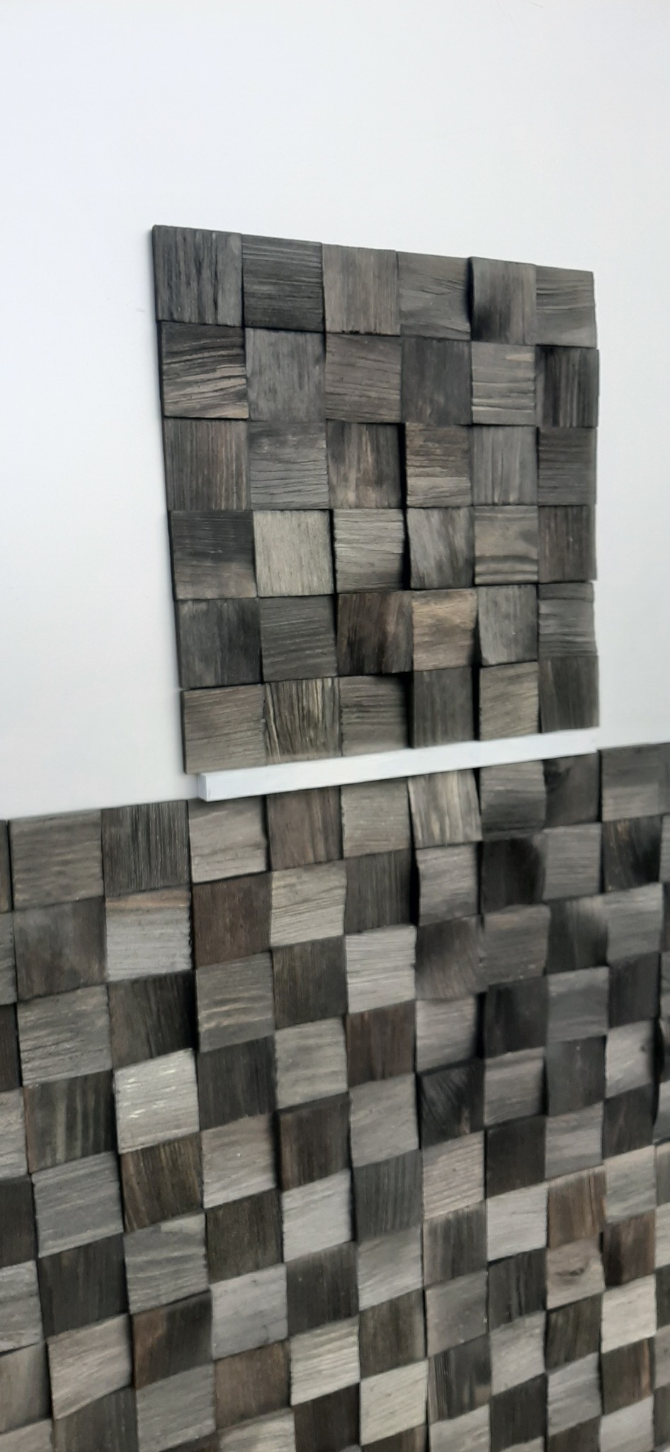Dekoracyjna ściana z drewnianych, szarych kostek ułożonych w szachownicę, z wyraźnym rysunkiem słojów i fakturą drewna.