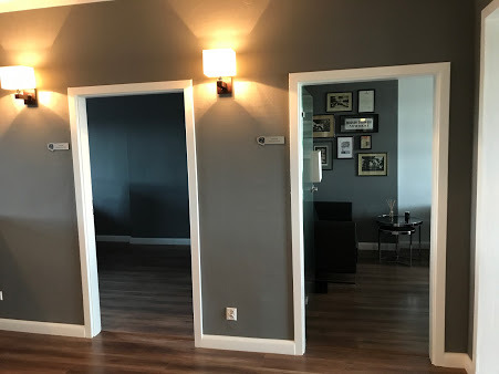 Wnętrze kancelarii z trzema parami drzwi z białymi futrynami, szare ściany z drewnianymi panelami oświetleniowymi, drewniana podłoga i galeria zdjęć w jednym z pomieszczeń.