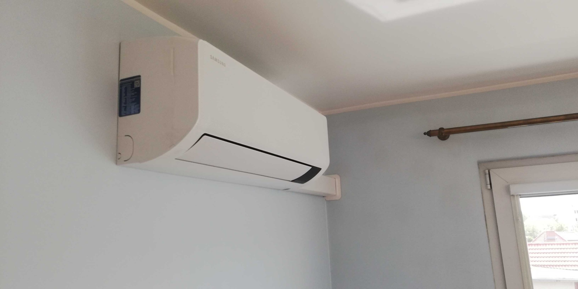 Zamontowany klimatyzator Samsung w jasnym wnętrzu mieszkania w Szczecinie, widoczna rama okienna i karnisz.