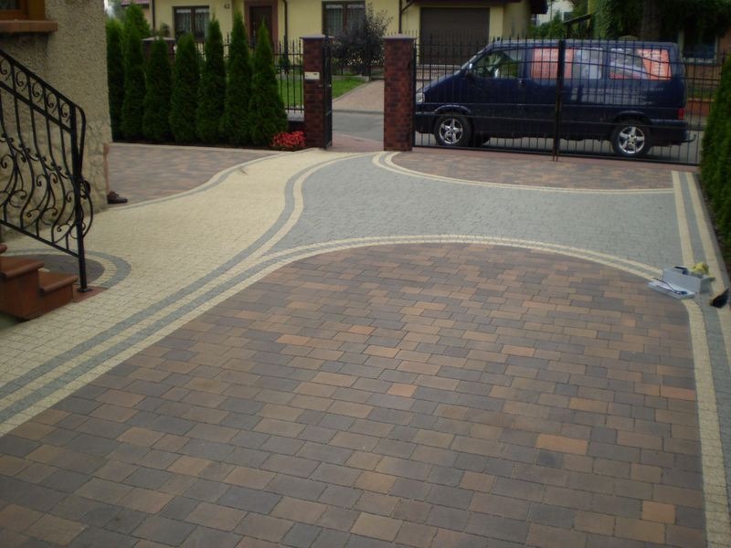 Kompozycja z wielobarwnej kostki brukowej na podjeździe w Jaworznie, zarysowana linia oddzielająca kolory, brama w tle z zaparkowanym vanem.