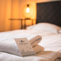 Piotr Widomski - Stos białych, puszystych ręczników z wizytówką Vistula Apartments na łóżku w pokoju hotelowym z oświetleniem w tle.