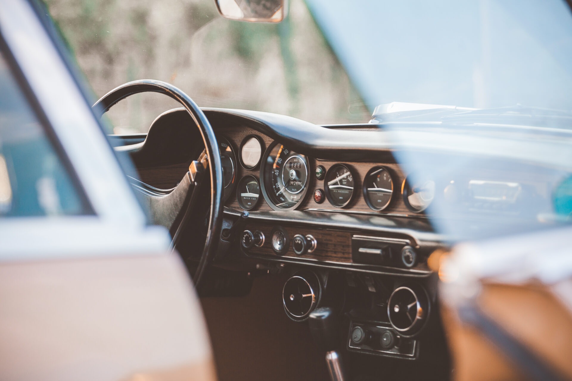 Wnętrze klasycznego samochodu Volvo z drewnianą deską rozdzielczą, widoczne zegary i kierownica, ujęcie przez szybę.