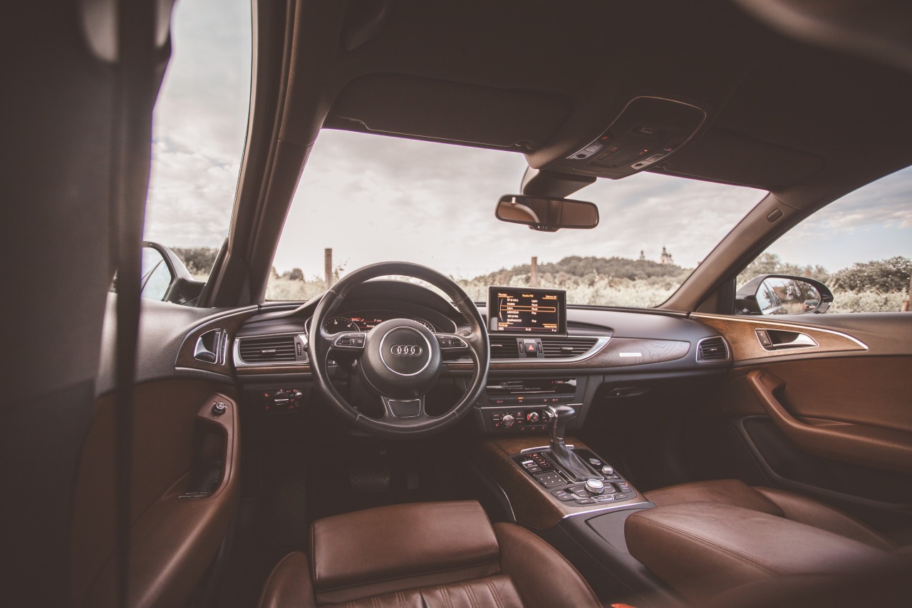 Wnętrze luksusowego samochodu Audi z brązową skórzaną tapicerką i drewnianymi elementami wykończenia, widok z perspektywy pasażera, w tle krajobraz z okolic Krakowa.