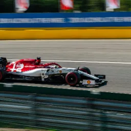Alfa Romeo Racing Orlen bolid F1 numer 42 pędzi po torze wyścigowym, widoczne logo sponsorów i ostre światło słoneczne.