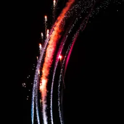 Akrobacje samolotu w Bydgoszczy z pirotechniką, tworzące barwne smugi na nocnym niebie.