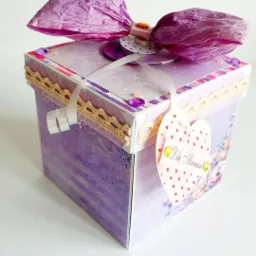 Ręcznie robione, fioletowe pudełko prezentowe z papieru z kokardą, koronką i zawieszką w kształcie serca z napisem 'Dla Mamusi'.