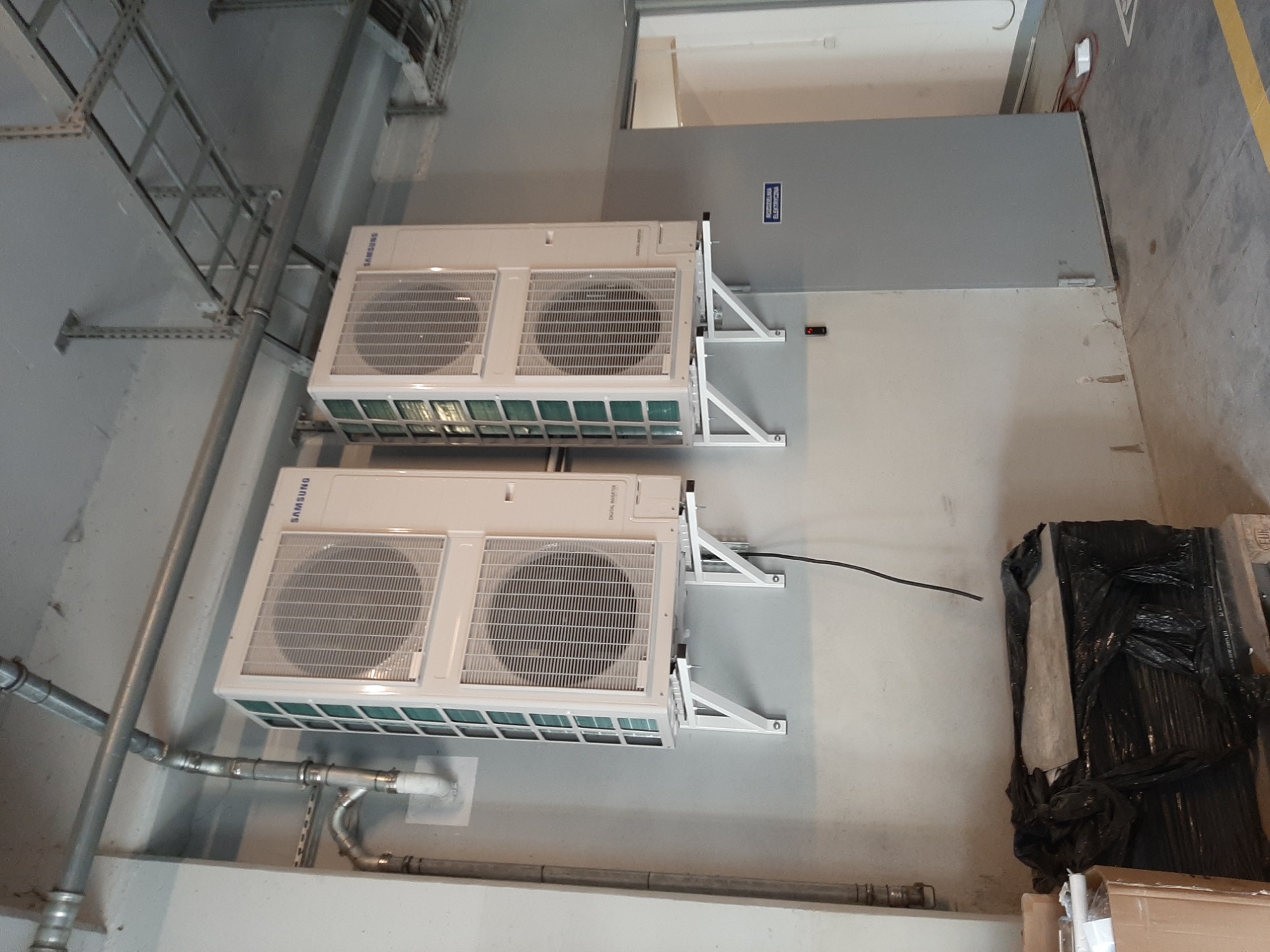 Dwa moduły klimatyzacji Samsung Digital Inverter zamontowane na ścianie w szarym pomieszczeniu technicznym, widoczne rury instalacyjne i metalowe konstrukcje wsporcze.