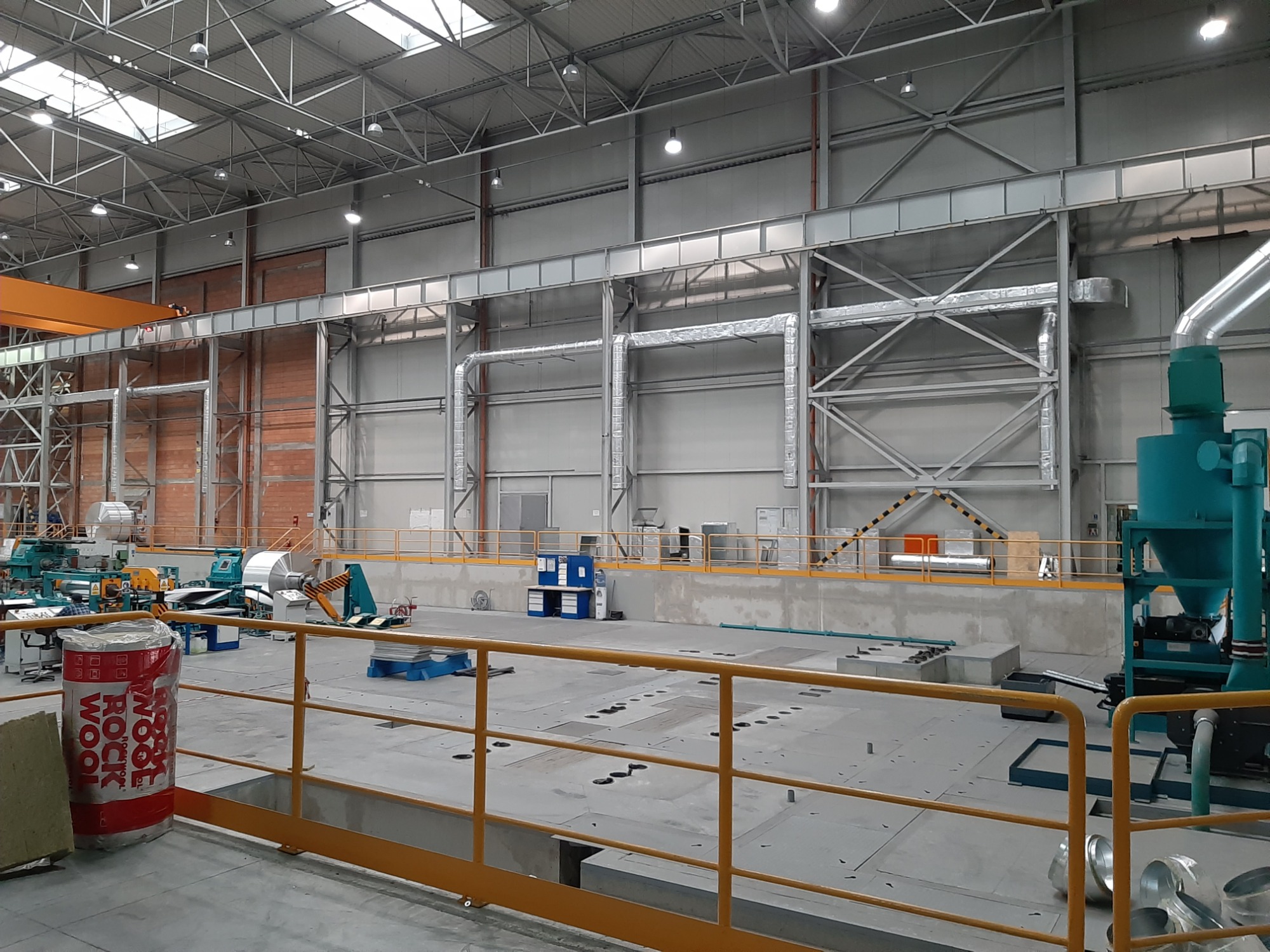 Wnętrze hali produkcyjnej z zainstalowaną, rozbudowaną instalacją wentylacyjną pod stropem, widoczne materiały izolacyjne Rockwool i elementy maszyn.