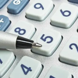 Zbliżenie na klawiaturę kalkulatora z metalowym długopisem wskazującym na cyfrę '5'.