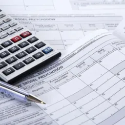 Formularz podatkowy PIT otwarty na stronie z tabelą, kalkulator i długopis leżą na wierzchu, gotowe do wypełnienia.