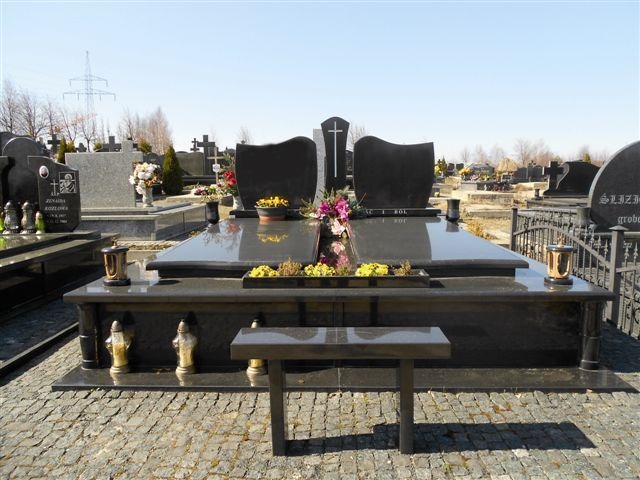 Czarny, podwójny nagrobek z kwiatami i zniczami na cmentarzu w Turze, na pierwszym planie mały stolik.