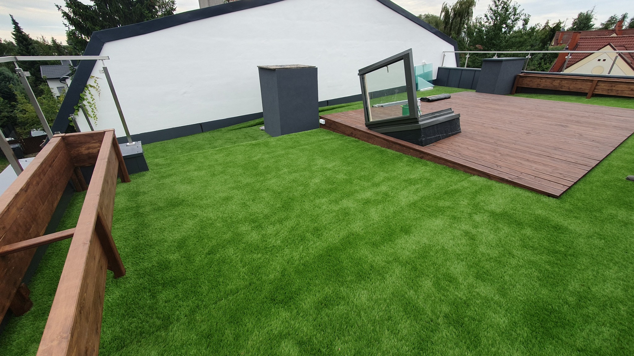 Zielony dach w Warszawie z syntetyczną trawą, drewnianym tarasem i skrzyniami na rośliny, widok z góry.