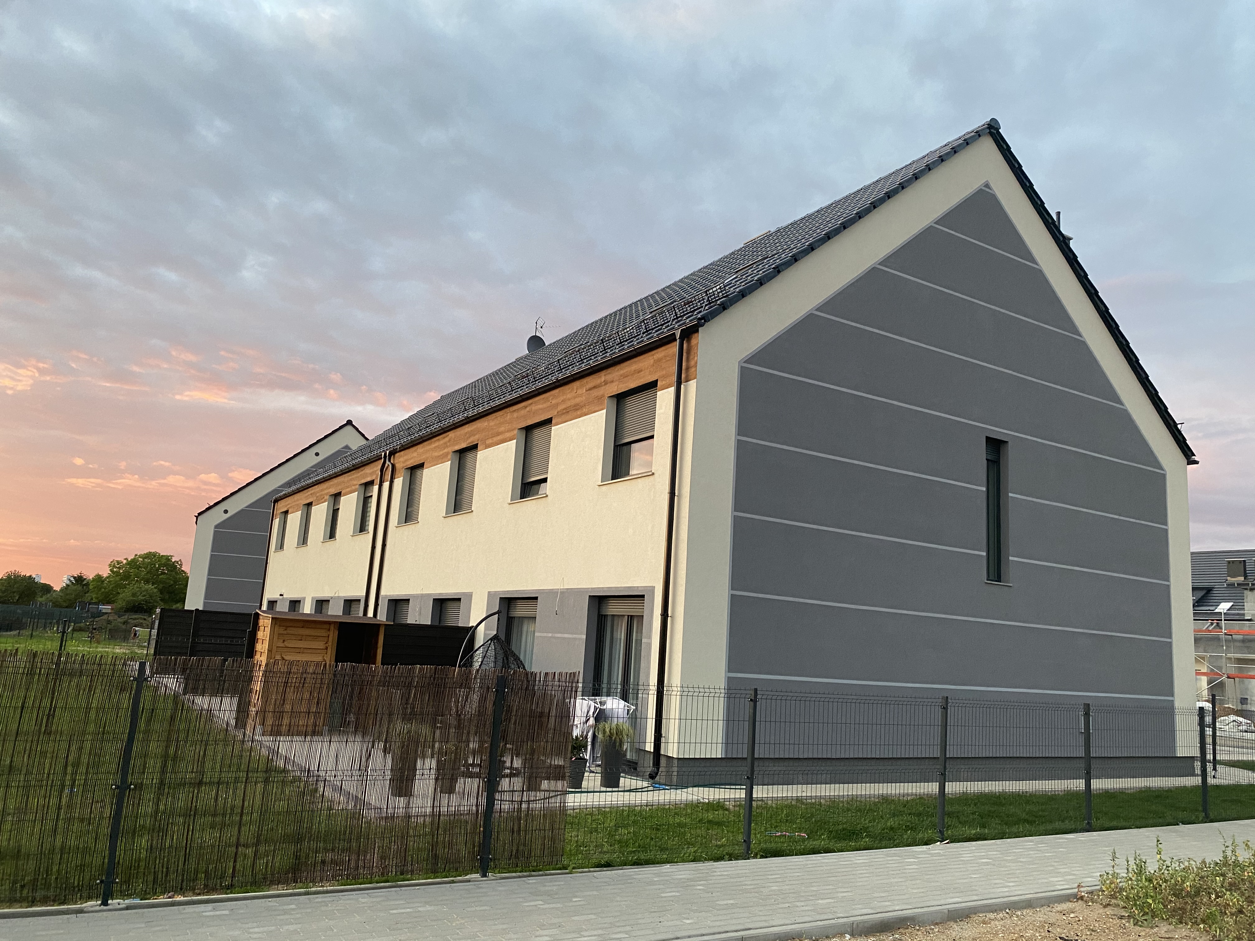 Nowoczesny budynek wielorodzinny z elewacją w odcieniach beżu i szarości, z poziomymi pasami dekoracyjnymi, sfotografowany o zmierzchu.