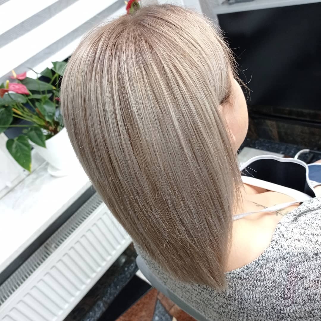 Włosy klientki po koloryzacji w odcieniach beżu i blondu, z precyzyjnym cięciem na prosto, widoczne z góry w salonie.