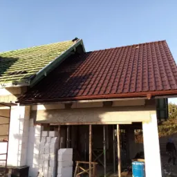 W trakcie montażu dachu z brązowej dachówki ceramicznej na nowym domu murowanym, widoczna więźba dachowa i częściowo ułożone pokrycie.