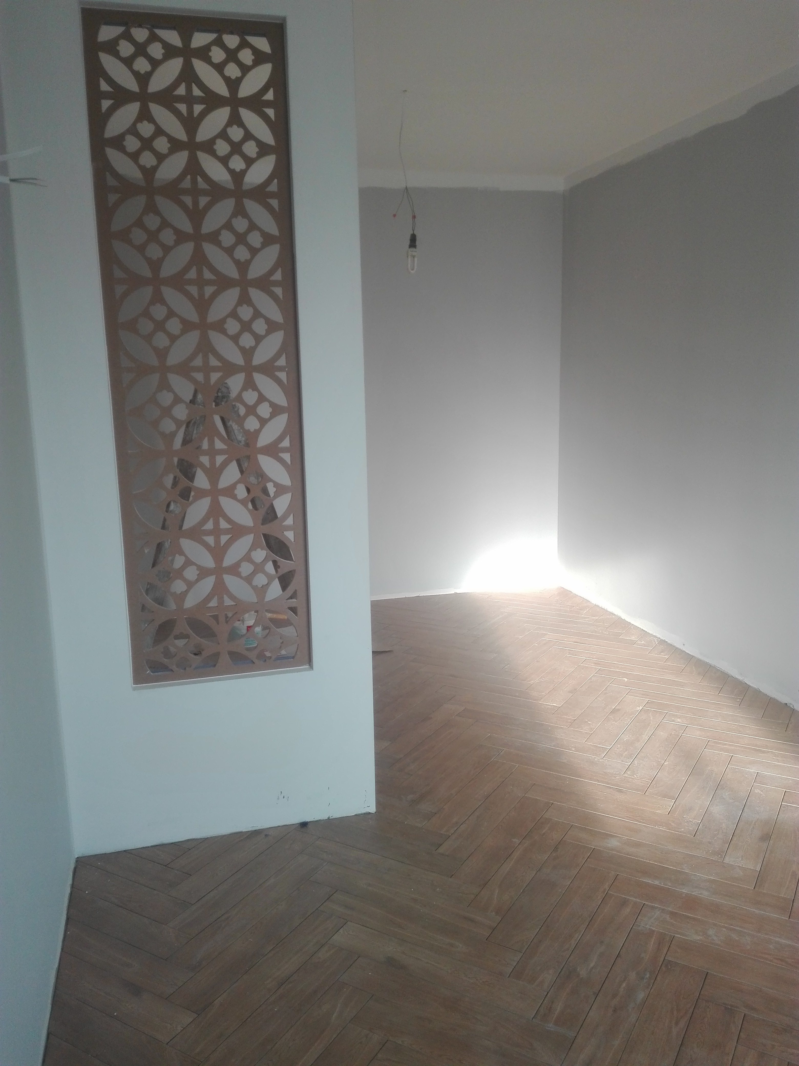 Ukończona podłoga z płytek ułożonych w jodełkę, widok zza dekoracyjnej ścianki działowej z ażurowym wzorem, surowy stan ścian w tle.